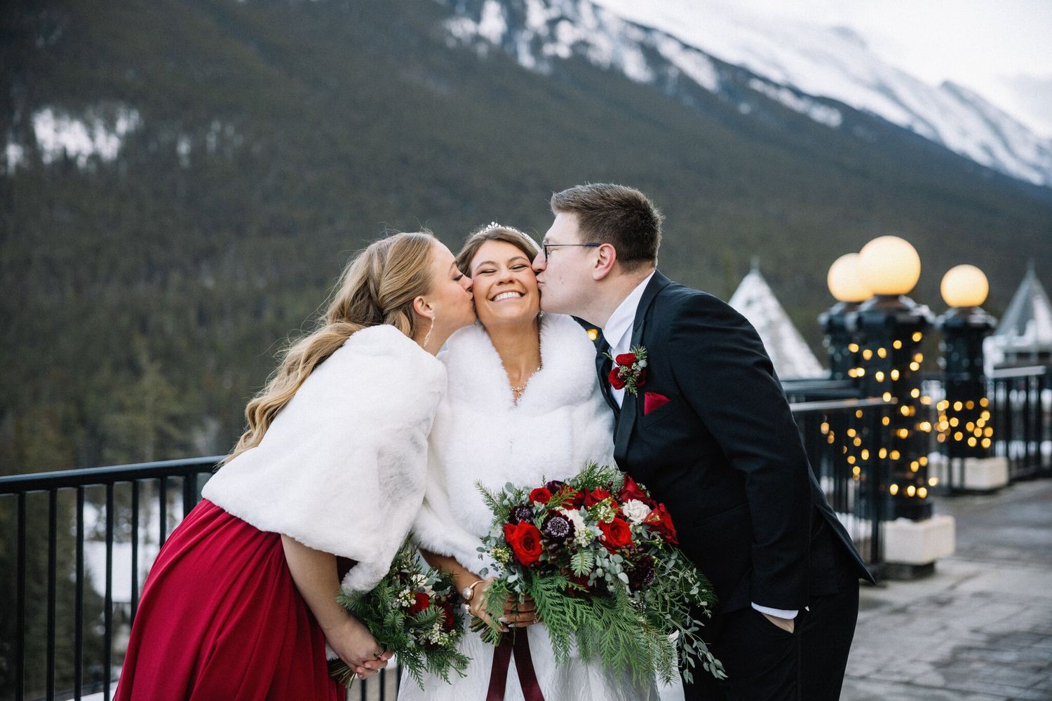 Bride laughs as two members of her wedding party kiss her cheeks on the terrace at her Banff Christmas wedding
