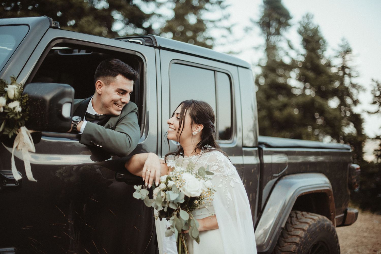 Black and white wedding photo of bride and groom gazing at each other outdoors among trees.