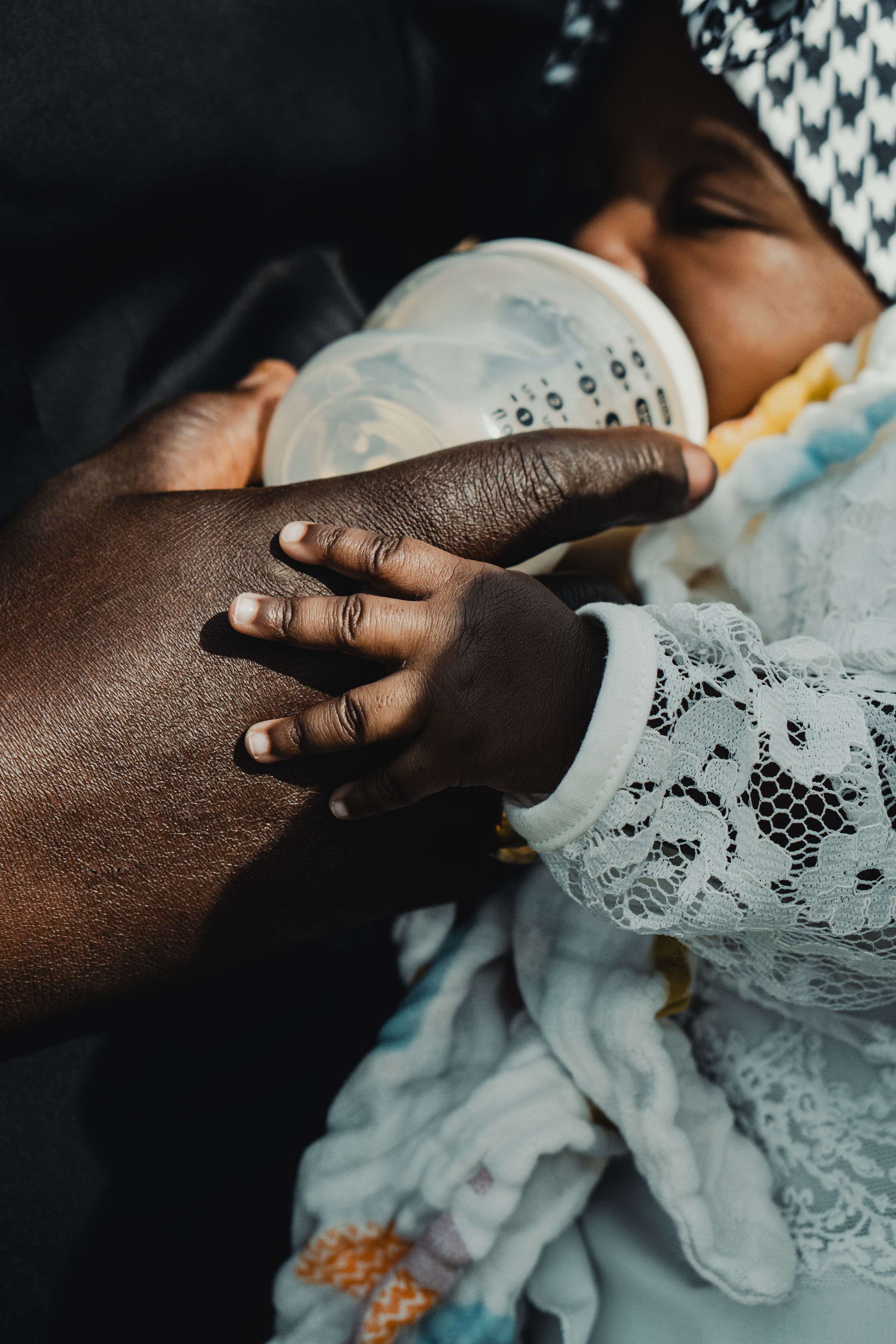 Close-up of a parent bottle-feeding a newborn baby, with the infant's tiny hand resting gently on the adult's arm.