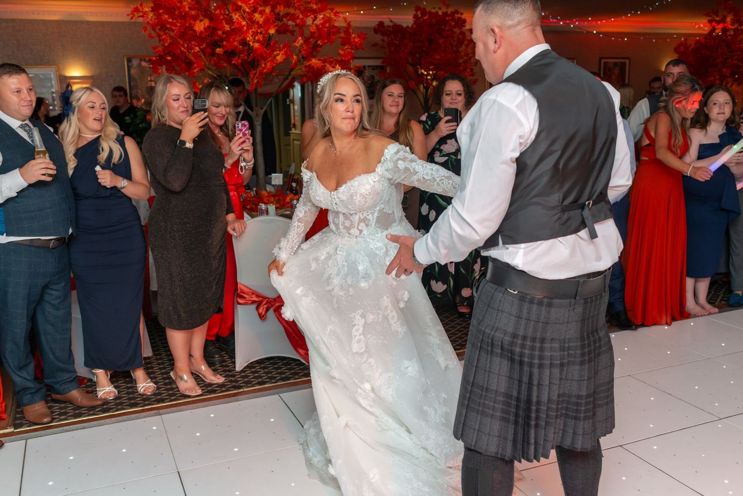 Emotional bride in white gown dances with groom in tartan kilt on white dance floor at wedding reception at Parklands, Widnes