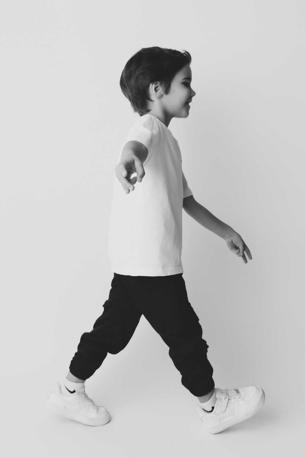 Black and white photo of a young boy walking in white t-shirt, black joggers, and white Nike sneakers.