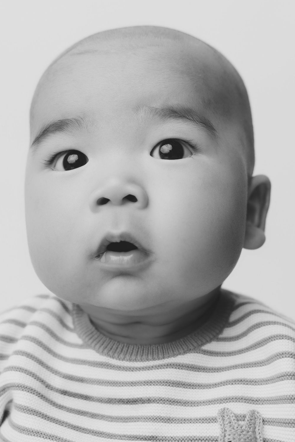 Black and white portrait of a curious Asian baby in a striped sweater looking up.