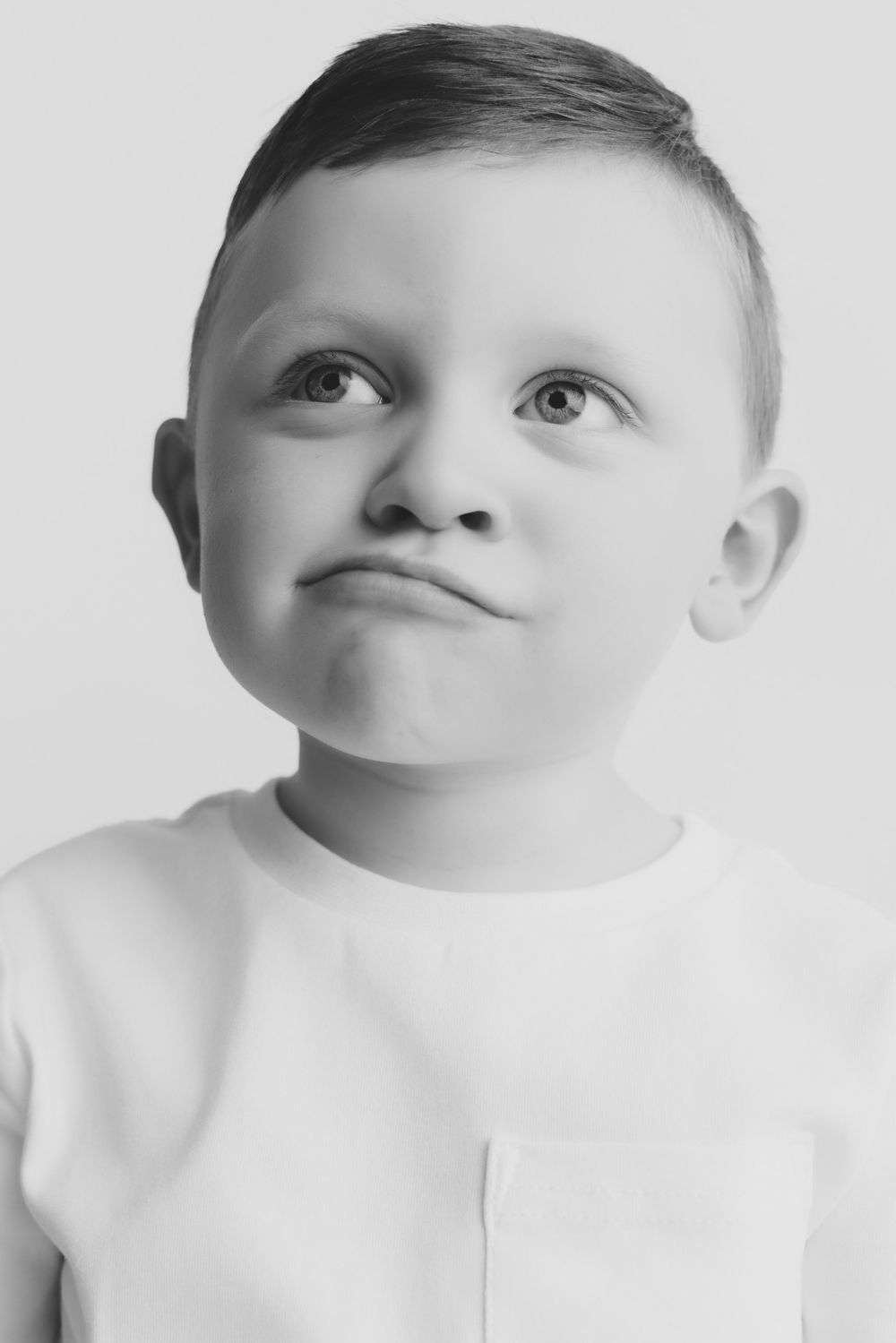 Black and white portrait of a young boy in a white shirt making a funny face while looking up.