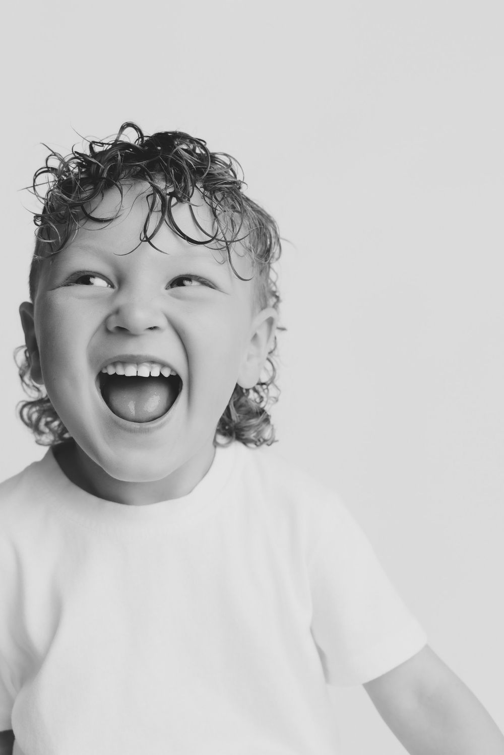 Black and white portrait of a joyful young boy with curly hair laughing and looking up.