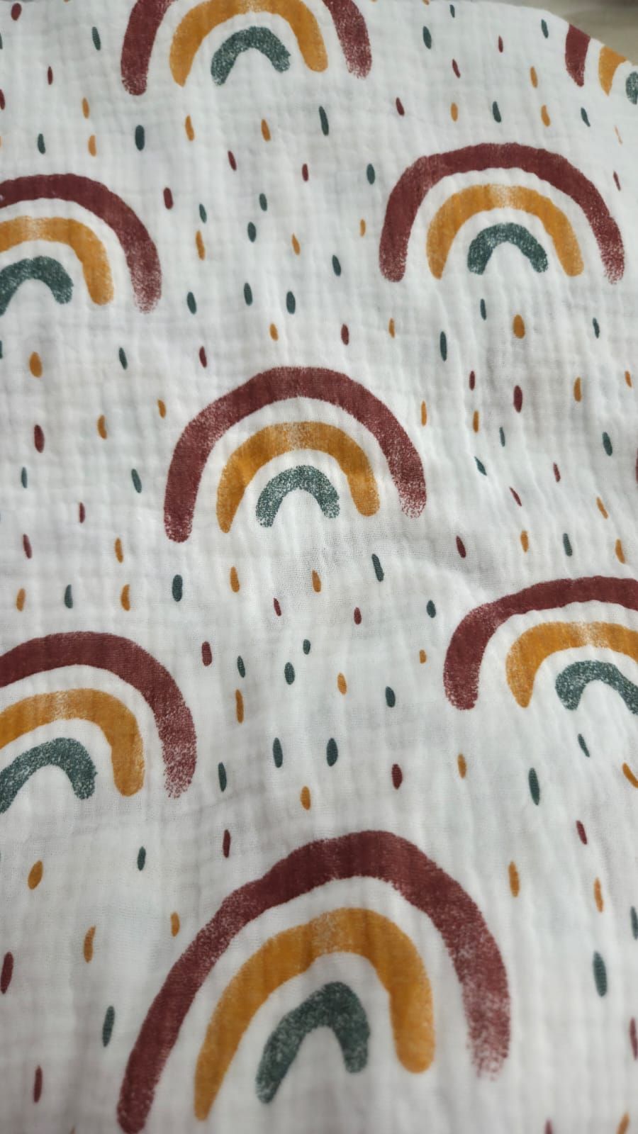 White muslin fabric with boho rainbow and colorful rain drops pattern in mustard, teal, and burgundy tones.