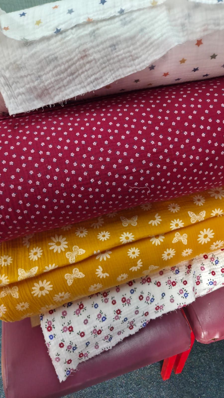 Stack of folded floral and butterfly print fabrics in red, yellow, white, and pink colors for sewing and quilting projects.