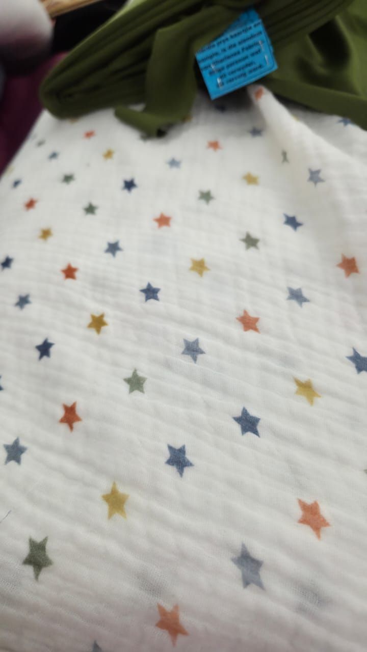 White muslin baby blanket with colorful scattered stars in blue, orange, green, and yellow on soft fabric.