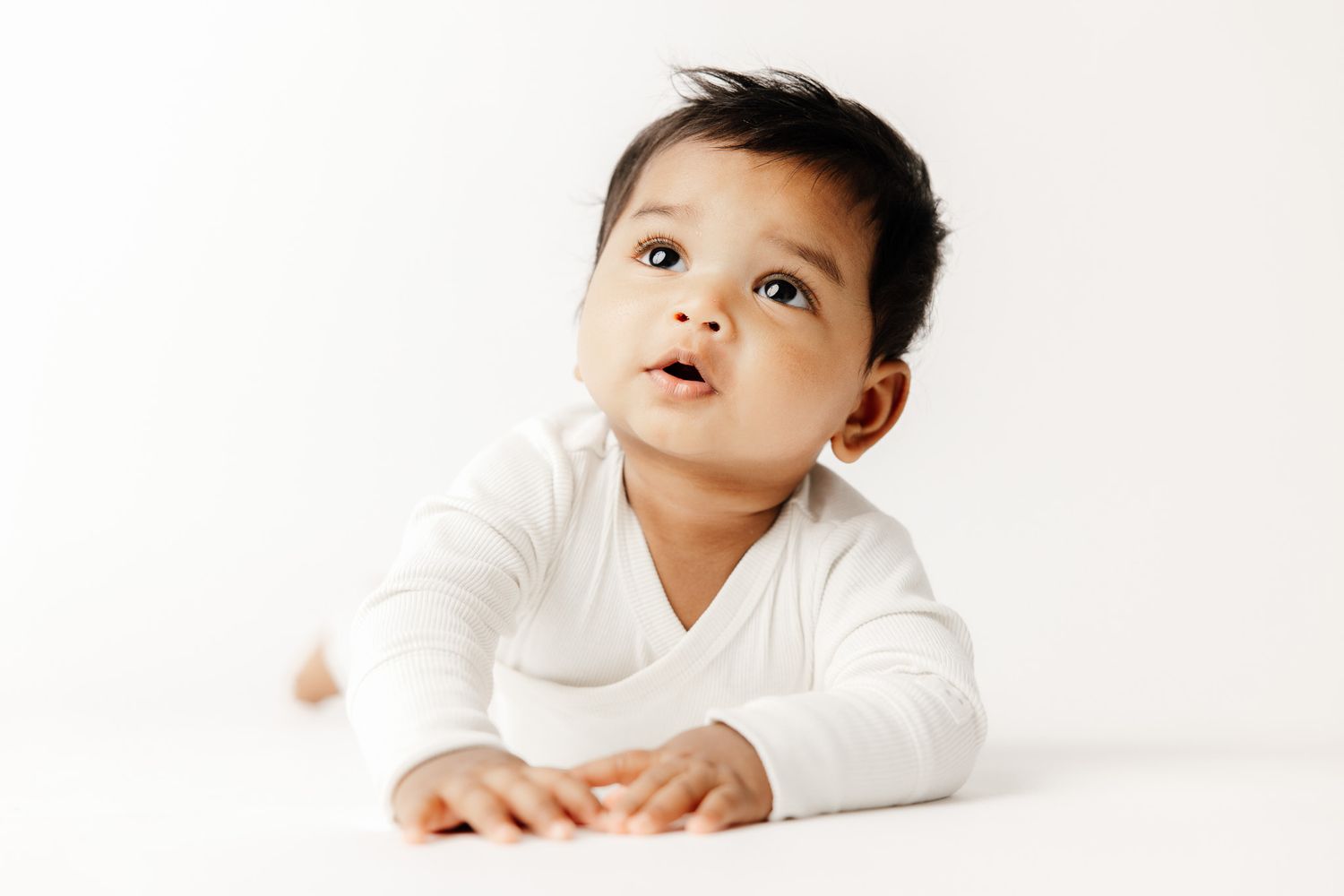 Peaceful newborn baby sleeping on white blanket, dark hair, soft skin, serene expression, professional newborn photography.
