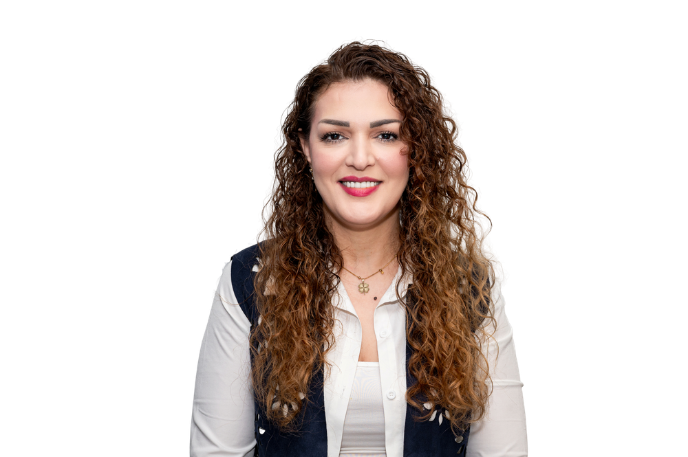 A smiling woman with curly brown hair wearing a white blouse and navy vest against a white background.