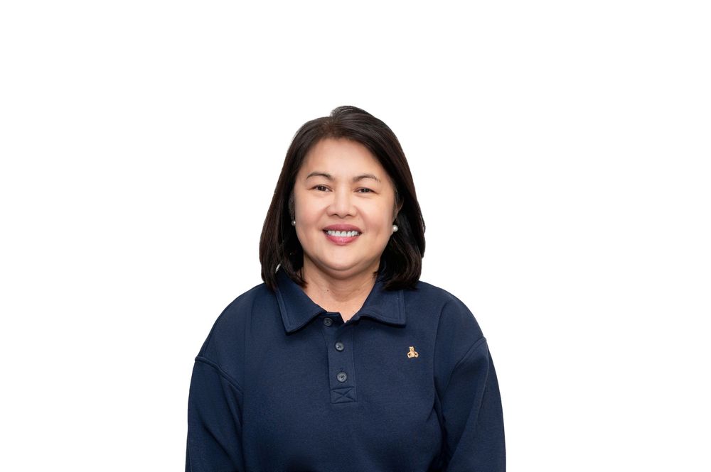 Smiling Asian woman in navy blue polo shirt with logo, professional headshot on white background.
