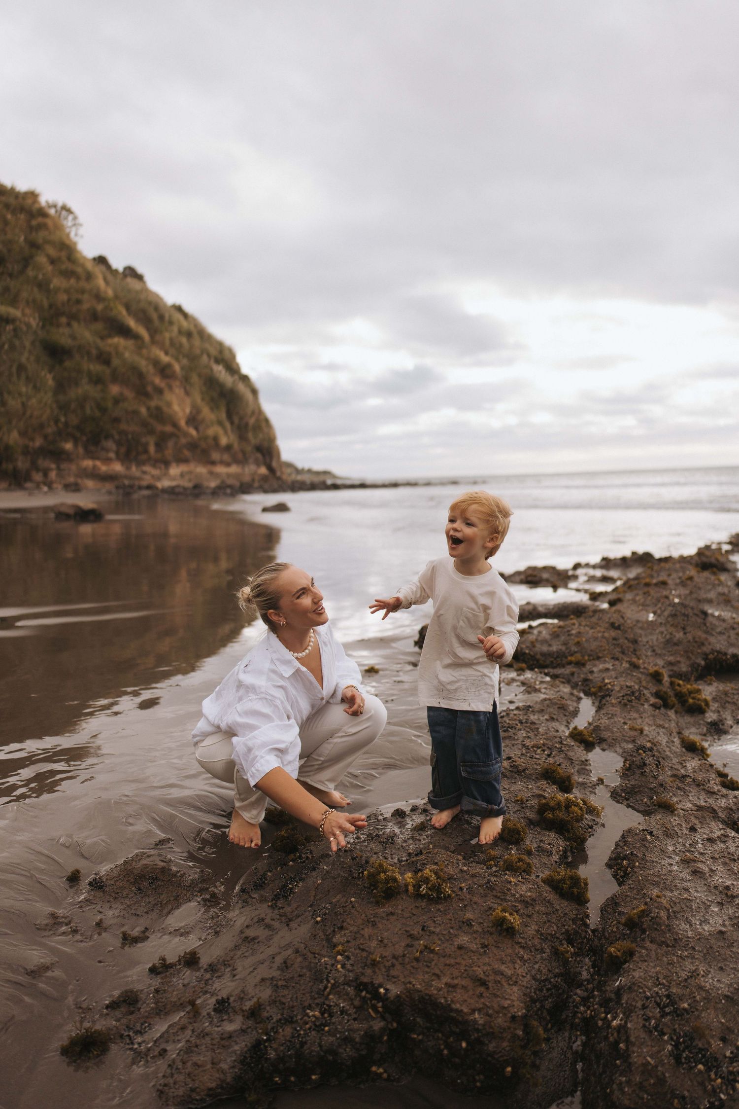 Mother laughing and playing with her toddler on a black sand beach in Raglan, New Zealand