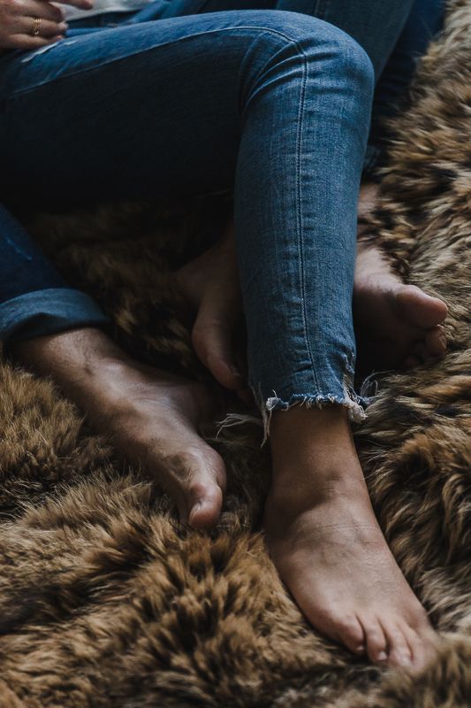 Bare feet and cuffed blue jeans rest on a soft brown faux fur blanket in a cozy close-up of a couple relaxing together.