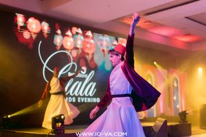 Whirling dervish performers in white robes and red hats dance on a stage at a gala awards evening with colorful lights and lanterns.