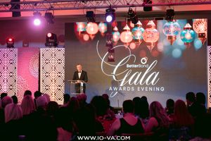 Speaker at a podium on stage during the BetterBond Gala Awards Evening, with colorful lanterns and an audience seated in the foreground.