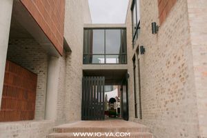 Narrow brick passageway between modern buildings with warm red and tan brickwork, wooden slatted gate, glass balcony above and stone steps.