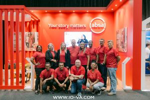 Team of smiling Absa employees in red shirts posing at a vibrant red exhibition booth with the slogan Your story matters.