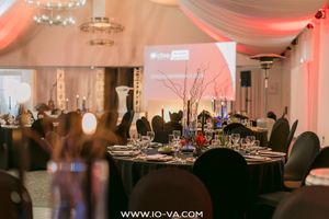 Elegant banquet hall with round tables, branch centerpieces, place settings, and draped ceiling fabric glowing in warm pink lighting.