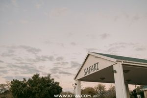 Safari-signed covered entrance with a green roof and white columns stands beneath a soft pink and gray twilight sky, with trees nearby.