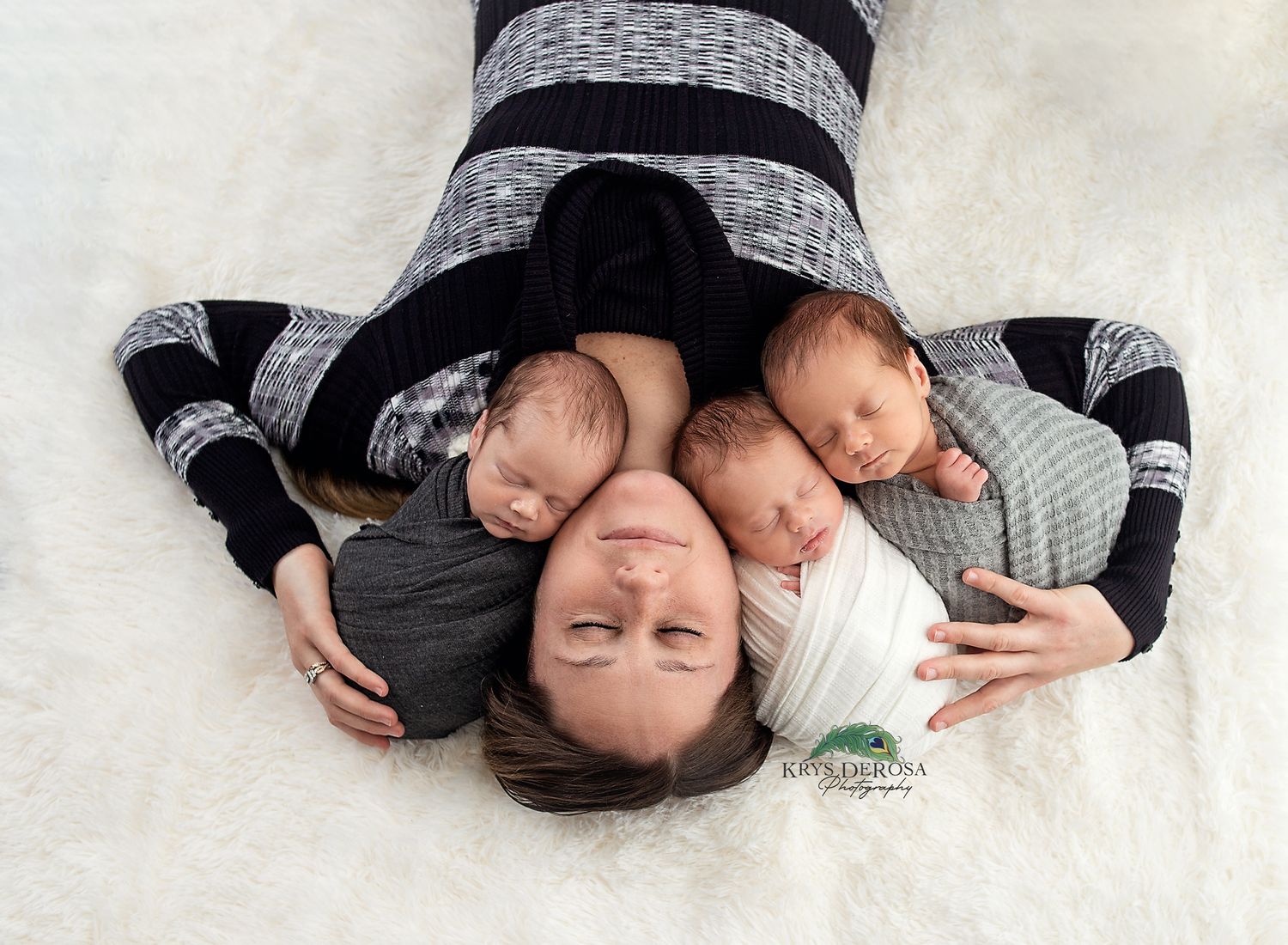 Mother lying down with three sleeping newborn triplets resting on her chest, captured in a professional newborn photography session.