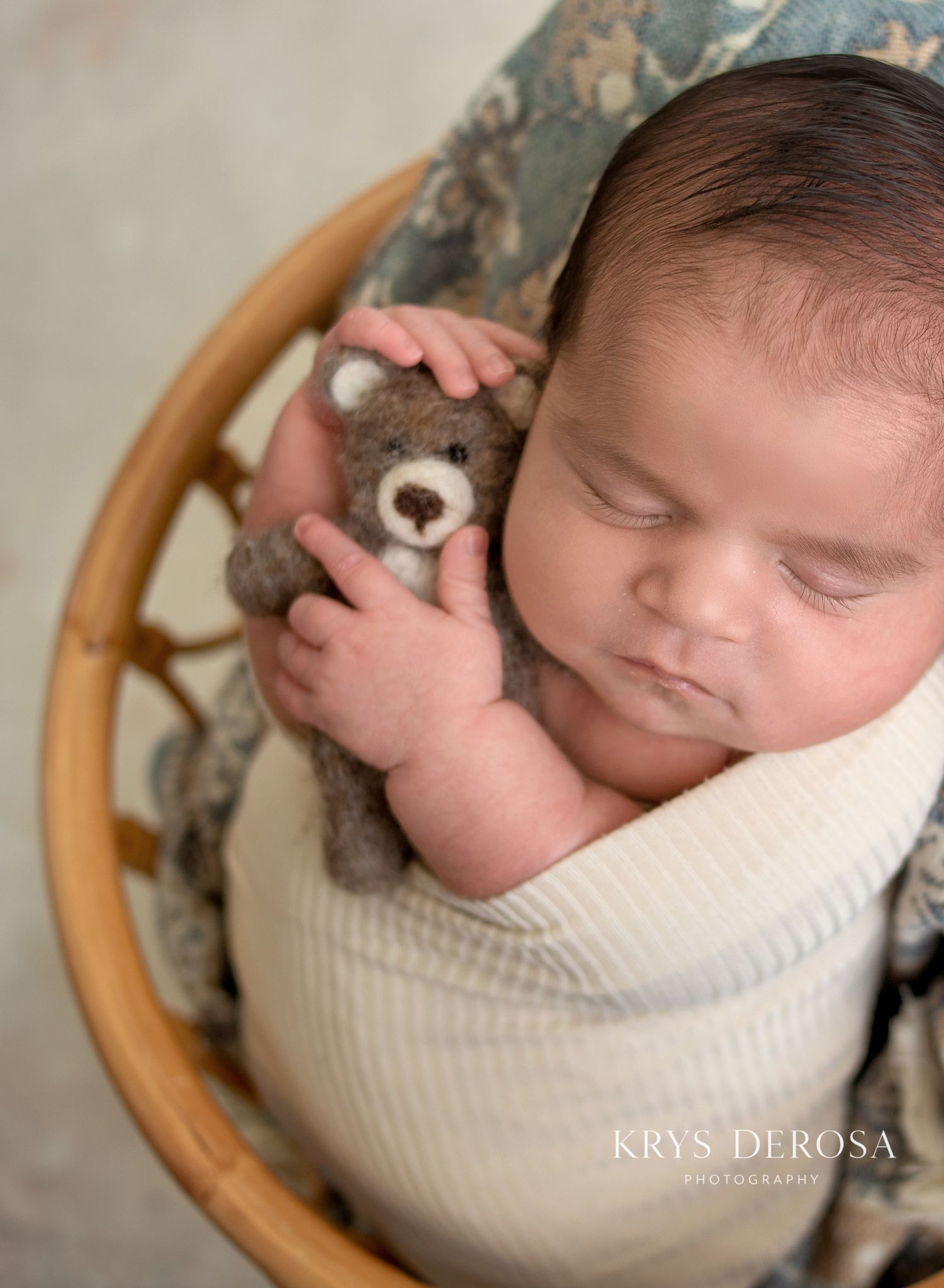 Sleeping newborn baby wrapped in white swaddle holding a tiny teddy bear in a wicker basket, professional photography.