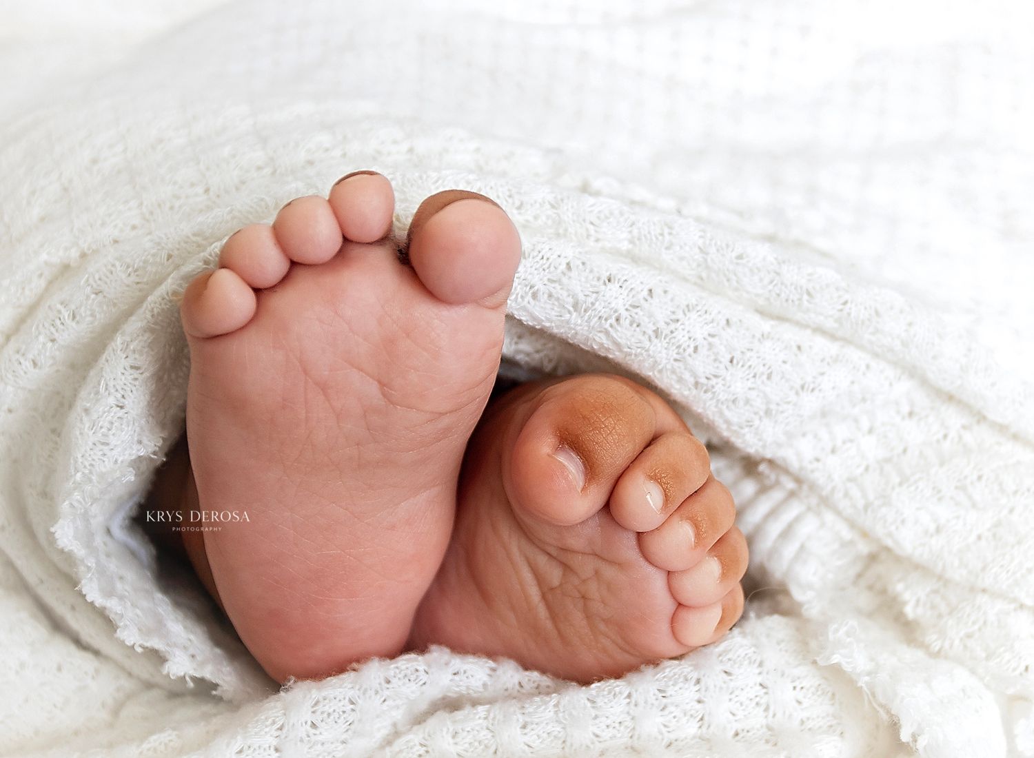 Close-up of newborn baby feet peeking out from a soft white knit blanket.