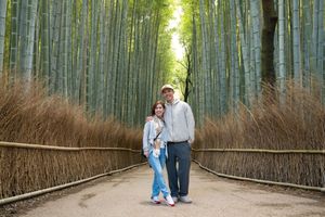 Couple posing together on a path between tall green bamboo stalks and woven bamboo fences in the Arashiyama Bamboo Grove.