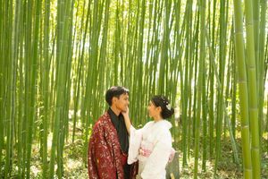 Couple in traditional Japanese kimono embracing among tall green bamboo stalks in a sunlit bamboo grove.