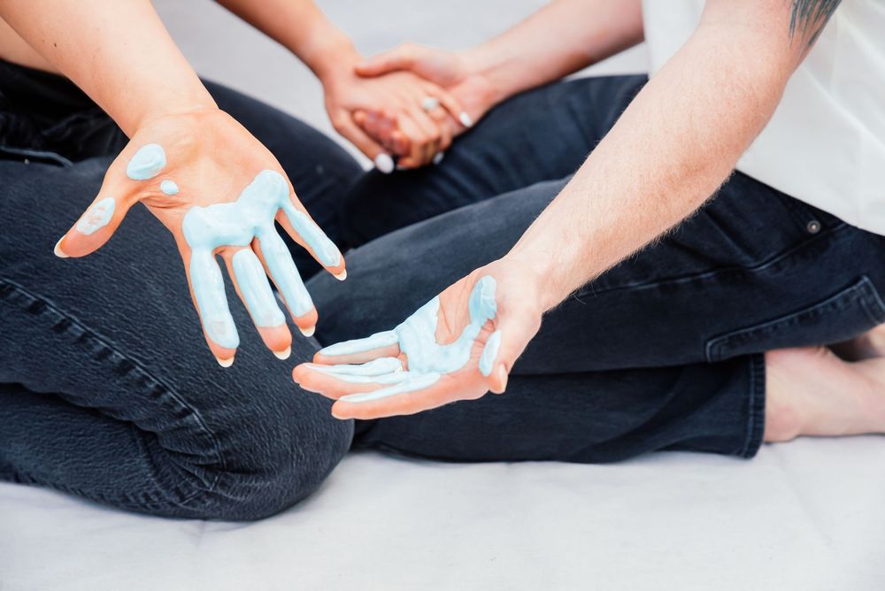 Two people with blue paint on their hands sitting cross-legged, sharing a creative and artistic moment together.