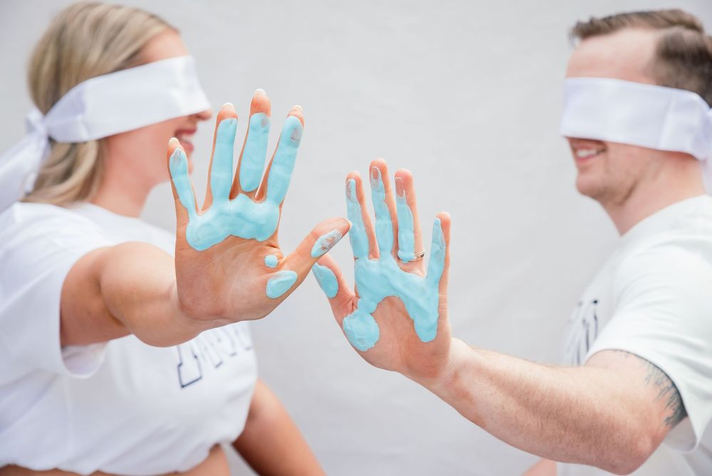 Blindfolded couple with blue paint on their hands facing each other in a fun outdoor activity.
