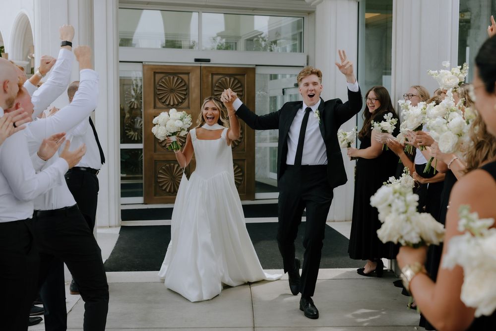 Joyful bride and groom exit church doors as wedding guests celebrate with white bouquets.