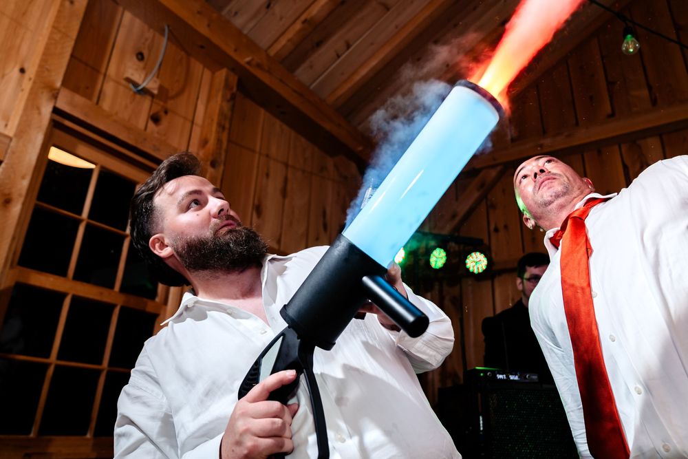 Wedding guests fire confetti cannon at lively barn reception celebration.