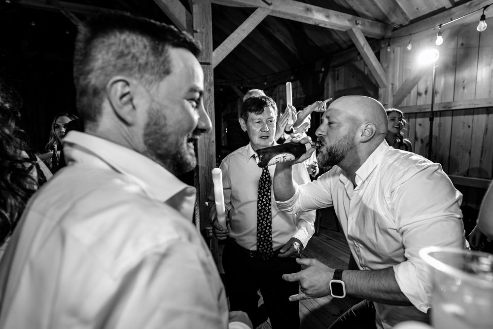 Groomsmen celebrating and drinking together at rustic barn wedding reception.