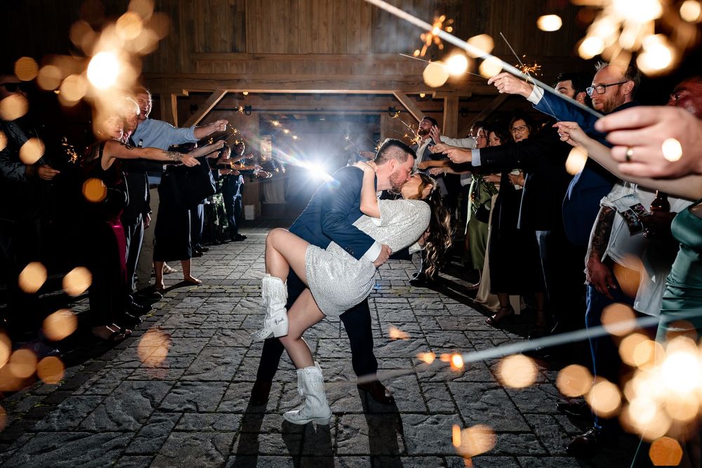 Couple kisses during sparkler send-off exit at barn wedding reception.