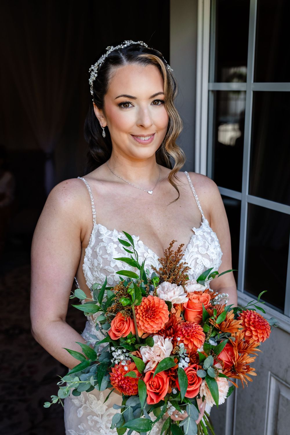 Bride in lace gown holding vibrant orange and red floral bouquet on wedding day.