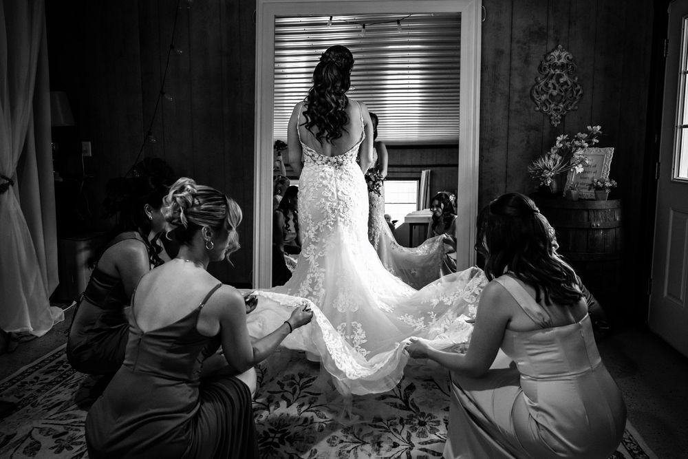 Bridesmaids helping bride with lace wedding gown train in black and white photo.