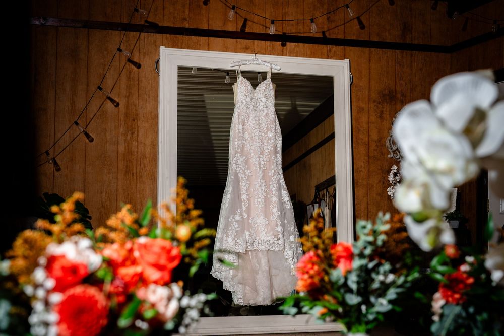 A lace wedding dress hanging in a doorway surrounded by vibrant orange and white floral arrangements.