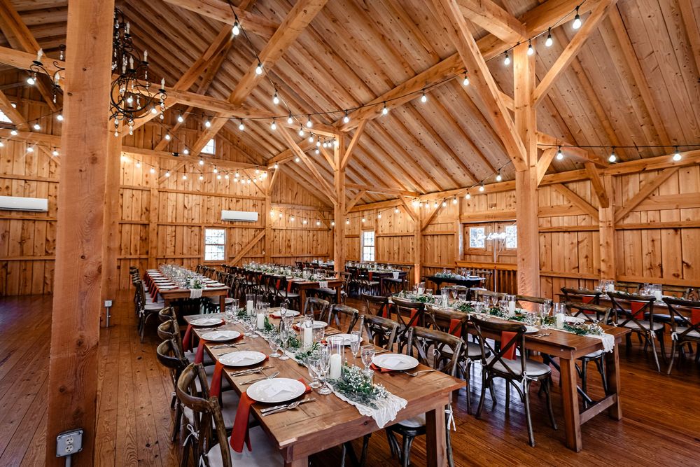 Rustic wooden barn reception venue with long farm tables, string lights, and elegant place settings.
