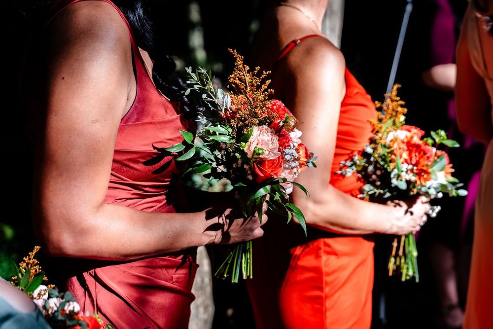 Bridesmaids in red dresses holding colorful autumn wedding bouquets with orange and red flowers.