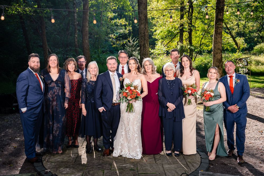 Wedding party and family group portrait outdoors at sunset in a wooded garden setting.
