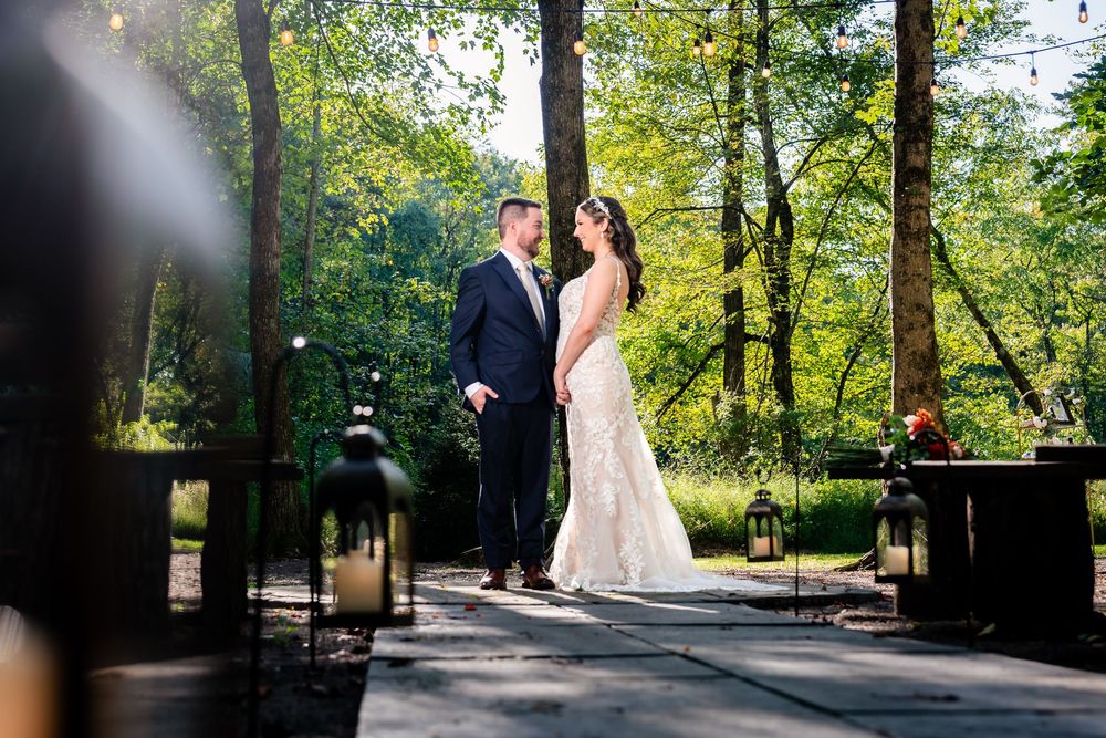 Bride and groom share a romantic moment on a sunlit outdoor patio surrounded by lush green trees.