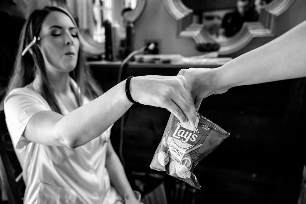 Black and white photo of a woman reaching for a bag of Lay's chips being handed to her indoors.