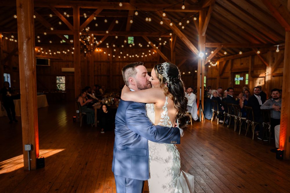 Bride and groom share romantic first dance under warm string lights in a rustic barn.