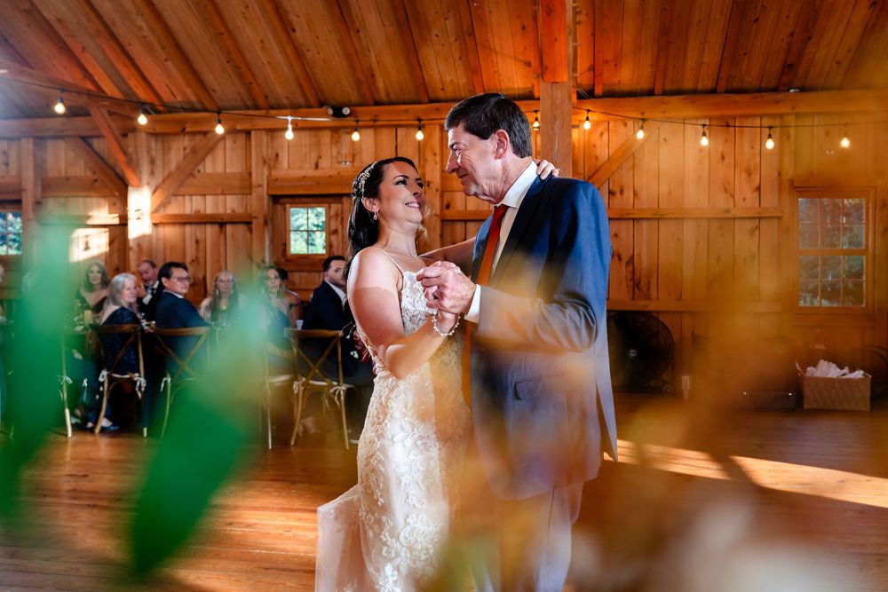 Bride and groom share their first dance in a rustic wooden barn venue with warm string lights.