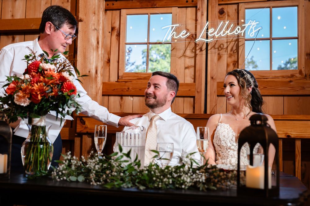 Father of the bride gives a heartfelt toast to the smiling newlyweds at the reception table.