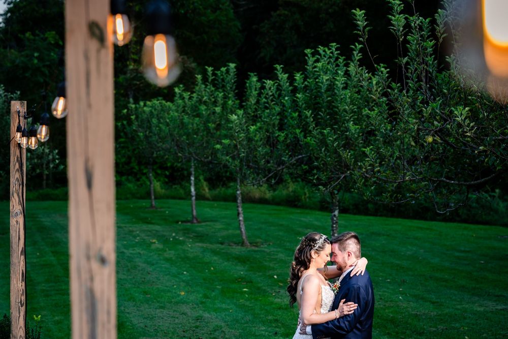 Bride and groom sharing romantic kiss under string lights at dusk outdoors.