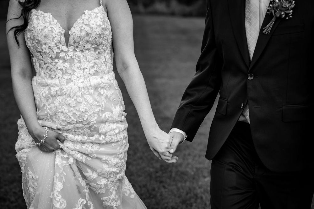 Black and white close-up of bride and groom holding hands showcasing lace wedding gown detail.