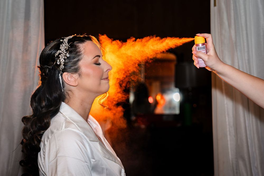 Bride getting hair sprayed with orange color mist during wedding preparation.