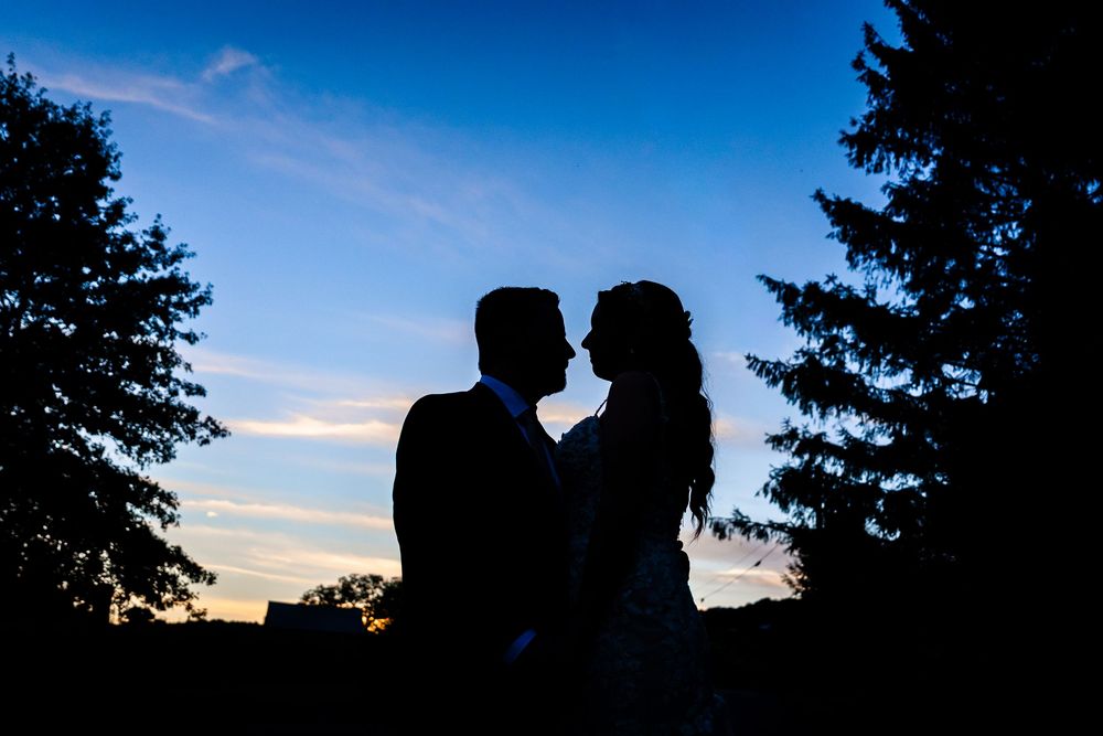 Romantic silhouette of bride and groom nearly kissing against a vibrant blue sunset sky.