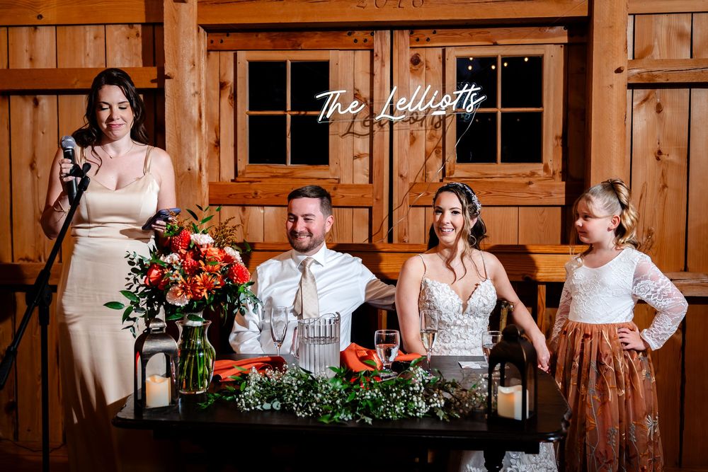 Maid of honor giving speech at rustic barn wedding reception with neon sign.