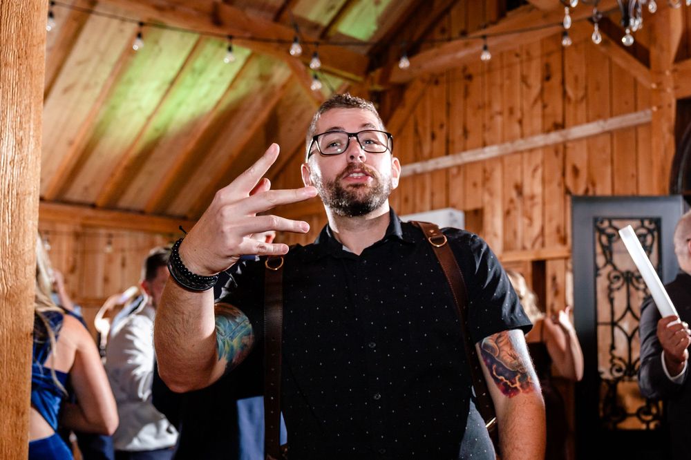 Tattooed guest in black shirt makes hand gesture at festive wedding reception.